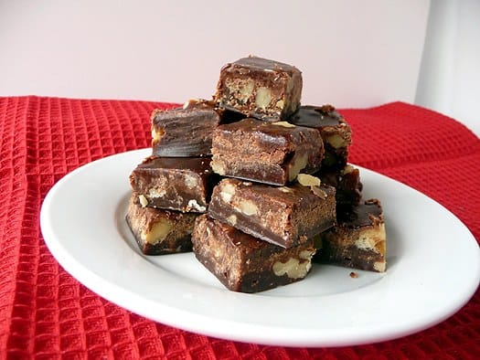 Squares of chocolate walnut fudge stacked on a white plate.