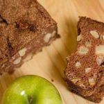 Overhead image of a loaf of apple cinnamon bread and one slice of it on a wood surface.