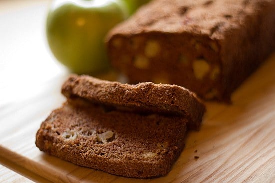 Loaf of apple cinnamon bread with 2 slices cut on a wood cutting board.