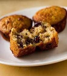 Oatmeal muffins with dates, cranberries, and pecans on a white plate with a bite taken from one muffin showing the inside texture.