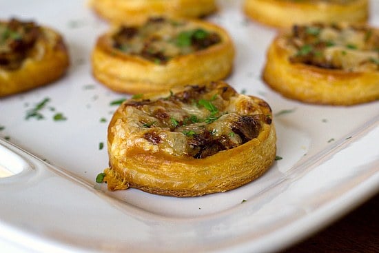 Side view of caramelized onion, mushroom, and gruyere tartlets on a white serving plate.