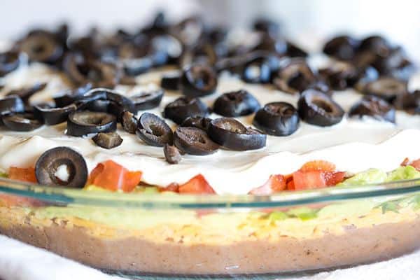 This Seven Layer Dip recipe is EASY and perfect for your Super Bowl party! Layers of refried beans, cheddar cheese, avocado, jalapeños, tomatoes, sour cream and olives! | browneyedbaker.com