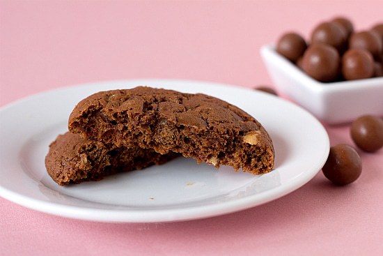 A chocolate malted whopper cookie broken in half on a white plate.
