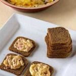 Hot reuben dip spread onto crackers on a white serving tray.