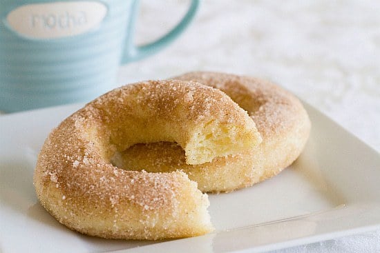 2 cinnamon sugar doughnuts on a white square plate with a bite taken from one.
