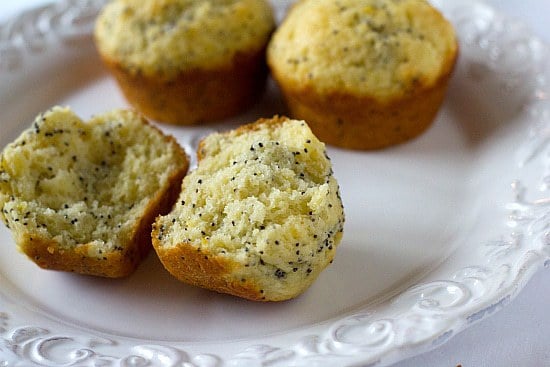 Lemon poppy seed muffins on a white plate with one muffin broken in half showing the inside texture.