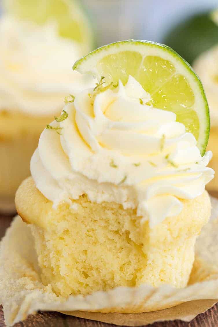 Margarita Cupcakes - A vanilla cupcake with vanilla frosting, lime zest and a lime wedge has a bite taken out of it.