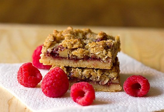 Stack of 2 raspberry streusel bars on a paper towel on a wood surface.