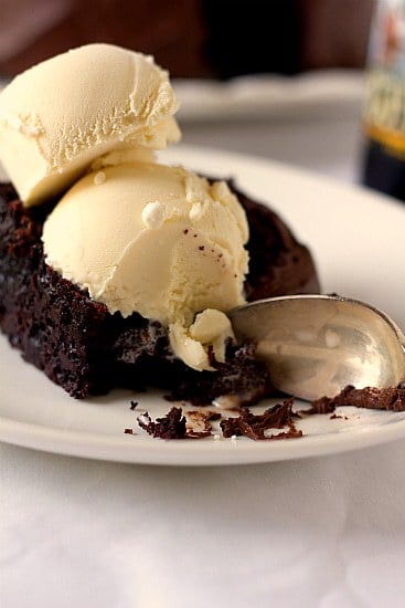A serving of root beer float cake on a white plate with a spoon topped with vanilla ice cream.