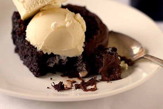 A serving of root beer float cake on a white plate with a spoon topped with vanilla ice cream.
