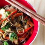 Soba noodle stir fry in a red bowl with chopsticks.
