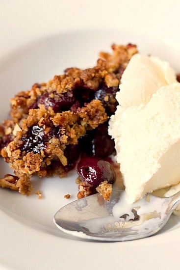 A serving of cherry crisp with vanilla ice cream in a white bowl with a spoon.