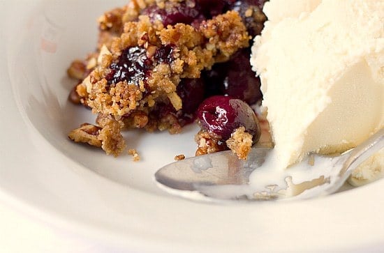 A serving of cherry crisp with vanilla ice cream in a white bowl with a spoon.