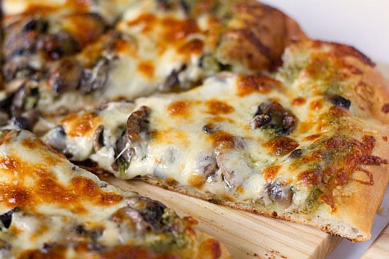 Slices of portobello pesto pizza on a wood cutting board.