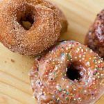 Overhead image of cinnamon sugar buttermilk doughnuts and glazed buttermilk doughnuts with nonpareil sprinkles on a wood surface.