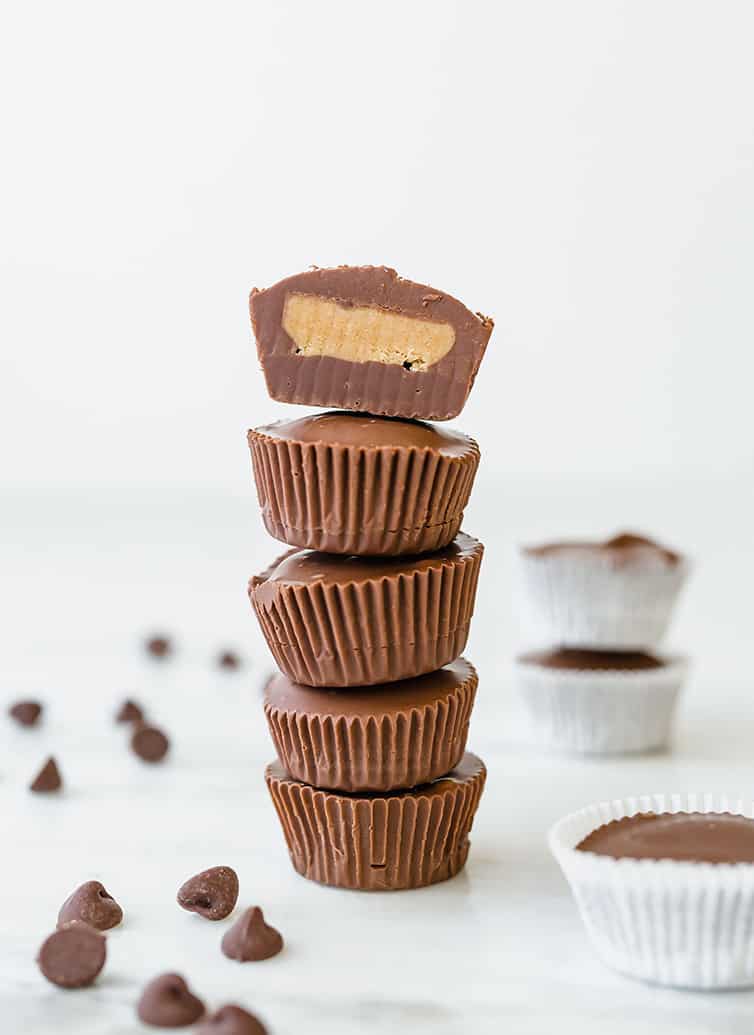 A stack of five peanut butter cups, with the top one sliced in half with filling exposed.