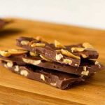 Stack of 3 pieces of caramel cashew bark on a wood board.