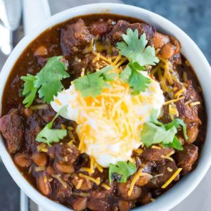 A bowl of chili con carne topped with sour cream, shredded cheese and cilantro.