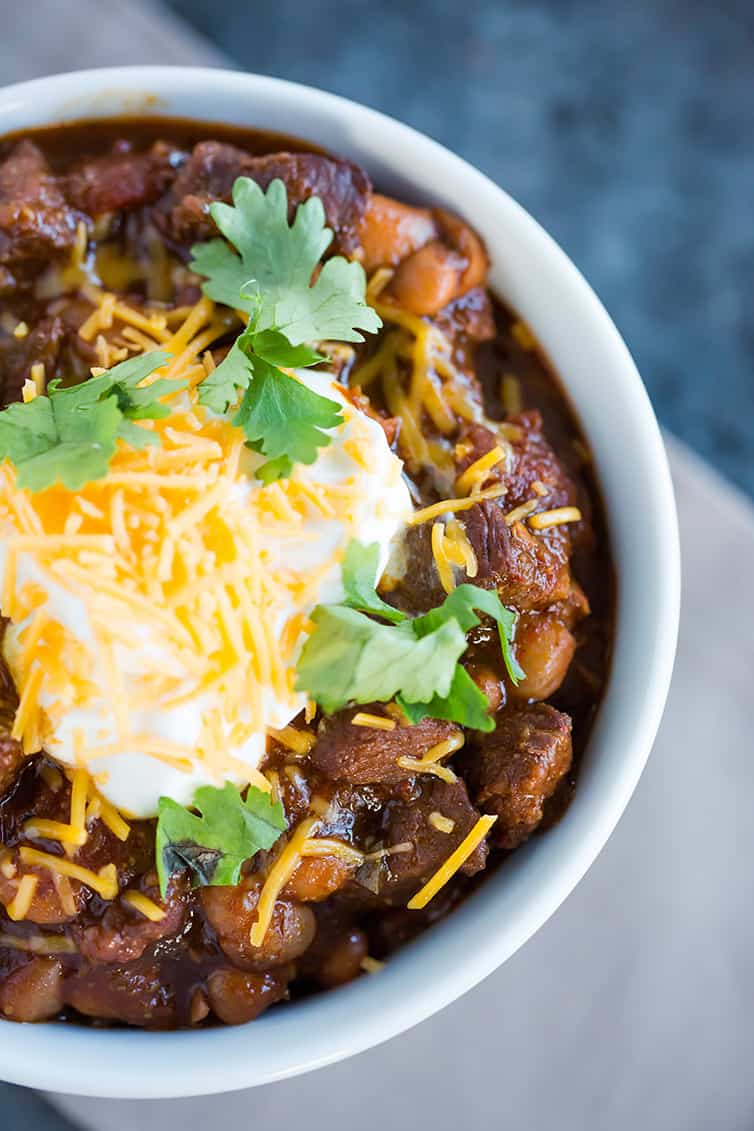 A close up shot of a bowl of chili con carne with sour cream, shredded cheese and cilantro on top.