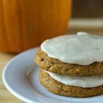 Stack of 2 pumpkin cookies topped with brown butter icing on a white plate.