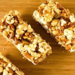 Overhead image of salted caramel popcorn, pretzel, and peanut bars on a wood board.