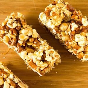Overhead image of salted caramel popcorn, pretzel, and peanut bars on a wood board.