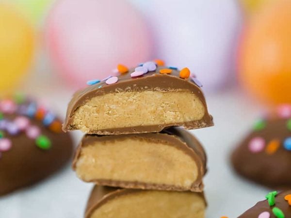 Peanut butter eggs, cut in half and stacked with Easter eggs in the background.