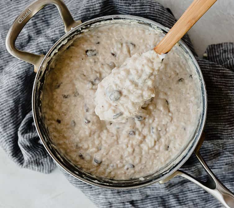 A batch of rice pudding in the pot with a wooden spoon lifting a spoonful out.