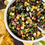 A bowl of black bean salsa with tortilla chips surrounding it.