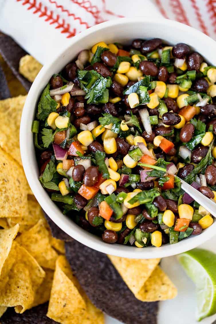 A bowl of black bean salsa with tortilla chips surrounding it.