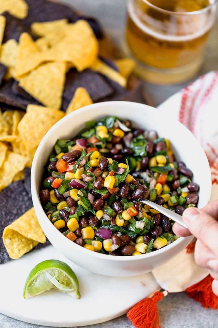 A bowl of black bean salsa with a hand scooping a spoonful.