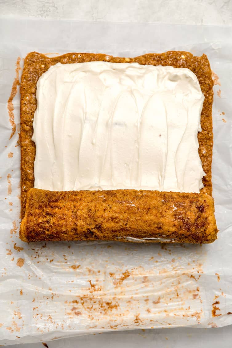 Pumpkin roll spread with cream cheese frosting and being rolled back up.