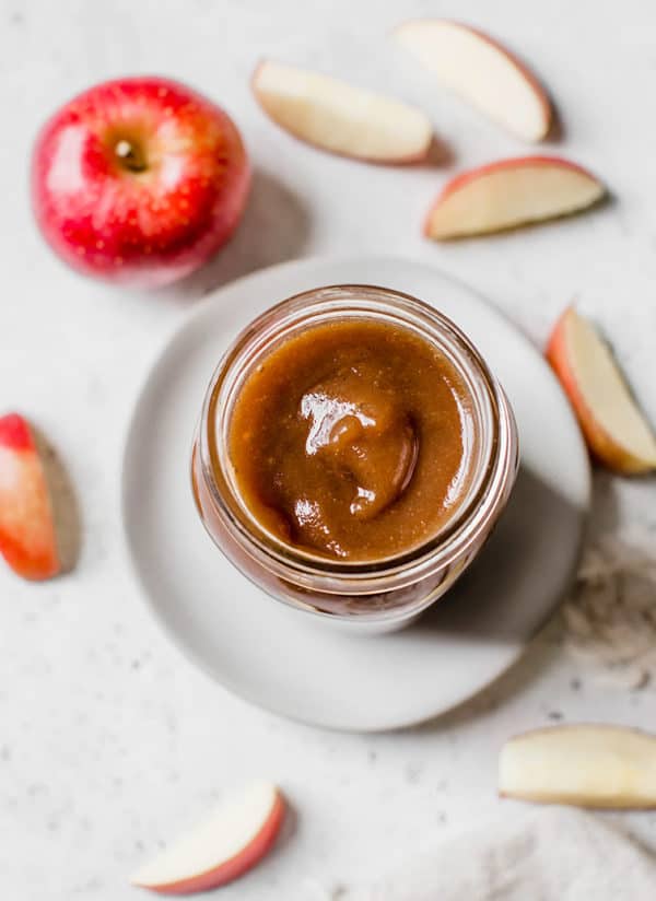 An overhead view of a jar of apple butter with sliced apples surrounding it.