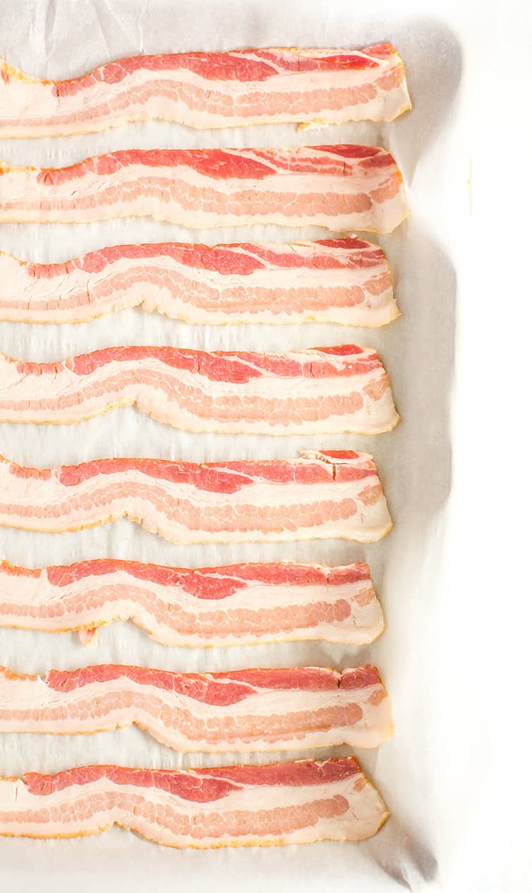 Slices of uncooked bacon on a parchment-lined baking sheet.
