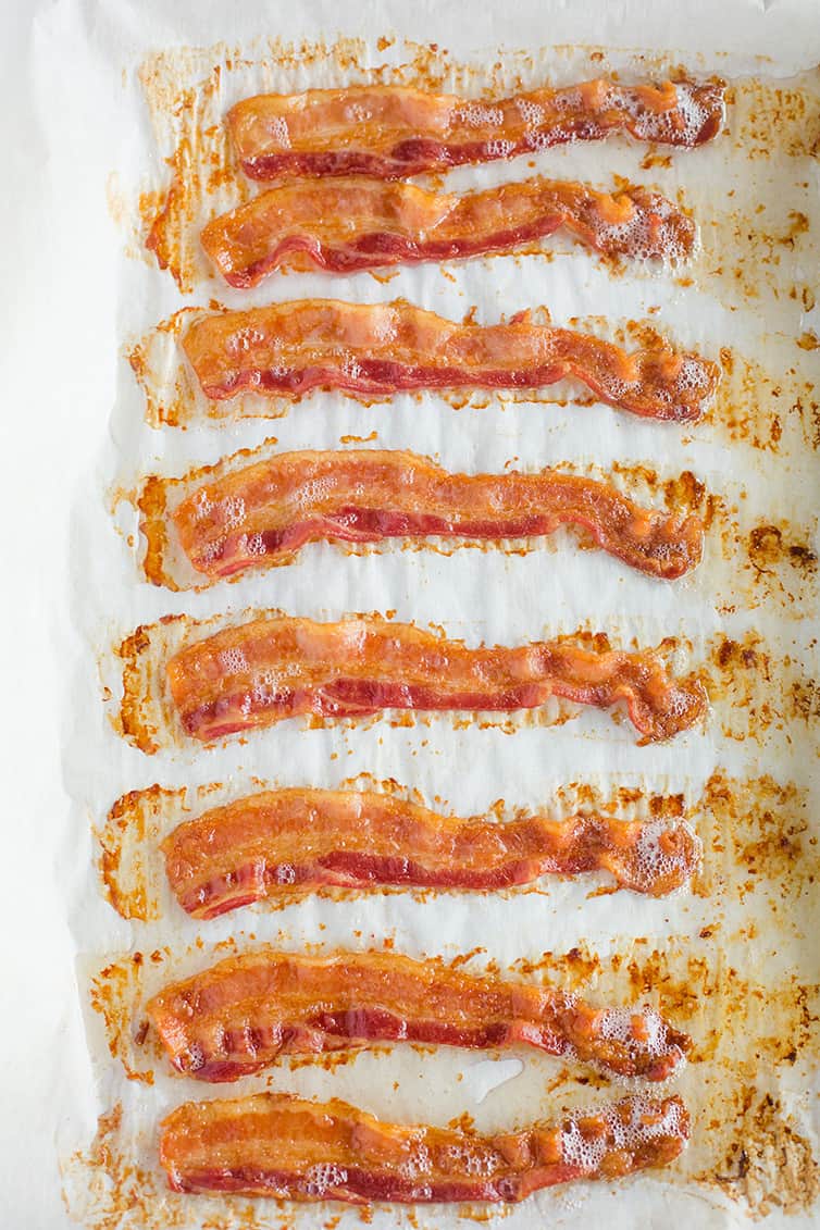 Freshly cooked oven baked bacon on a parchment-lined baking sheet.