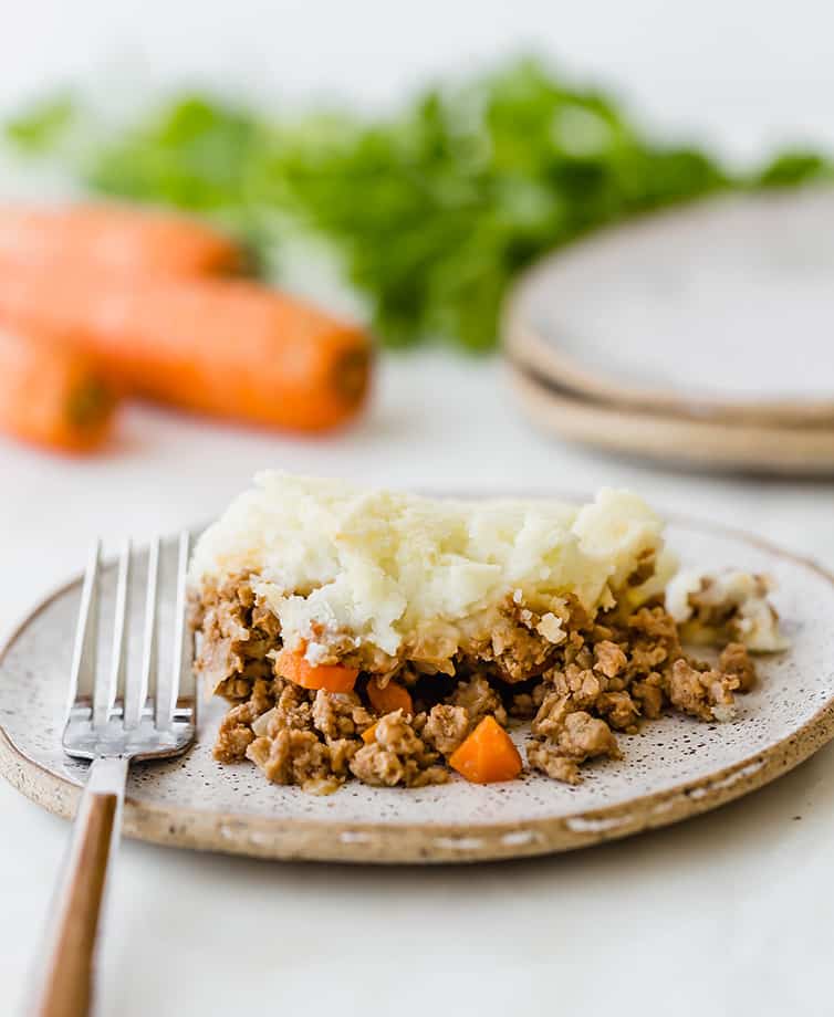A plate of shepherd's pie with carrots and parsley in the background.