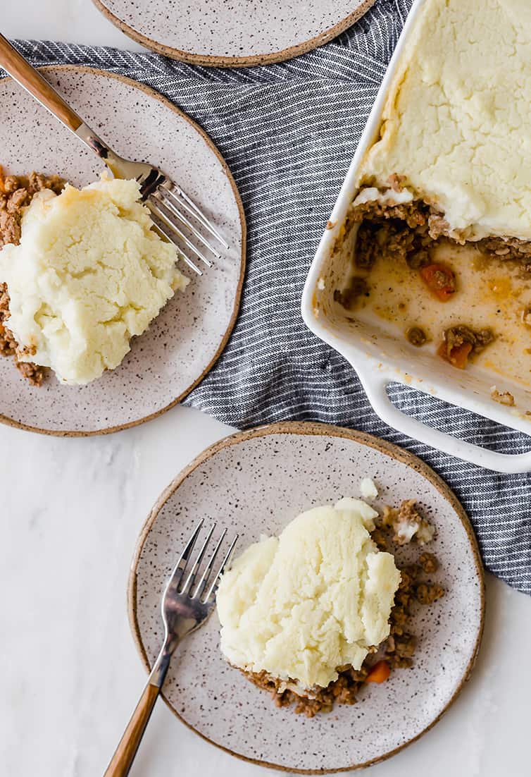An overhead shot of two plates of shepherd's pie and the casserole dish with servings scooped out.