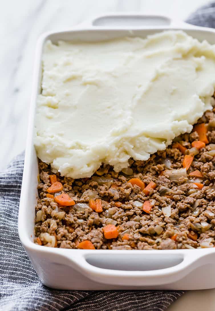 The meat mixture for shepherd's pie is in a casserole dish with the mashed potato topping being spread on top.
