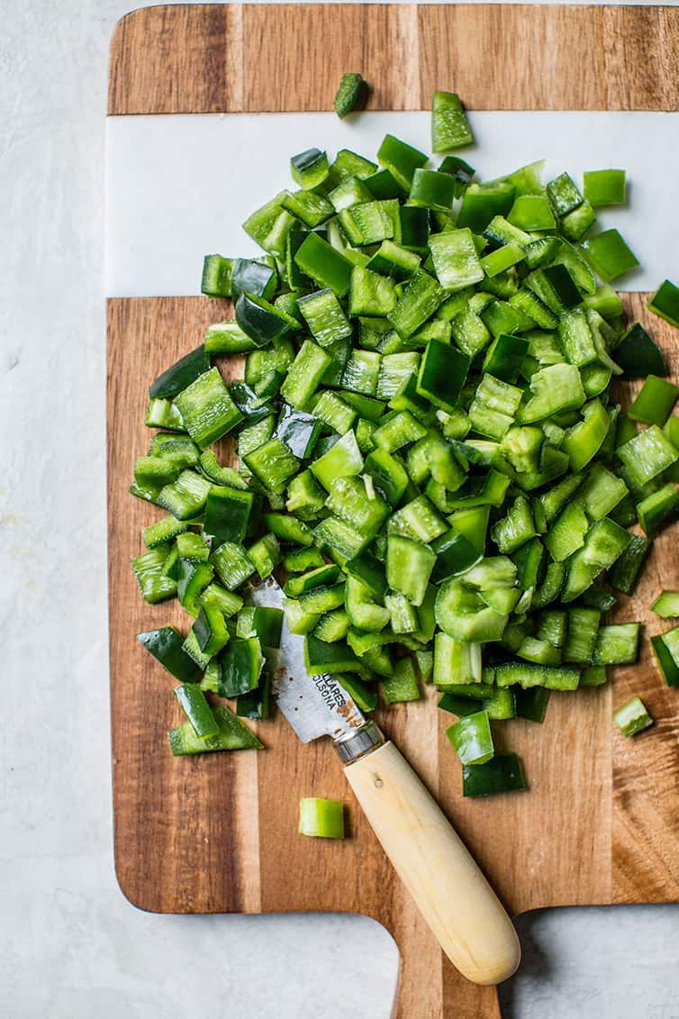 Chopped jalapeno and poblano peppers on a wooden cutting board.