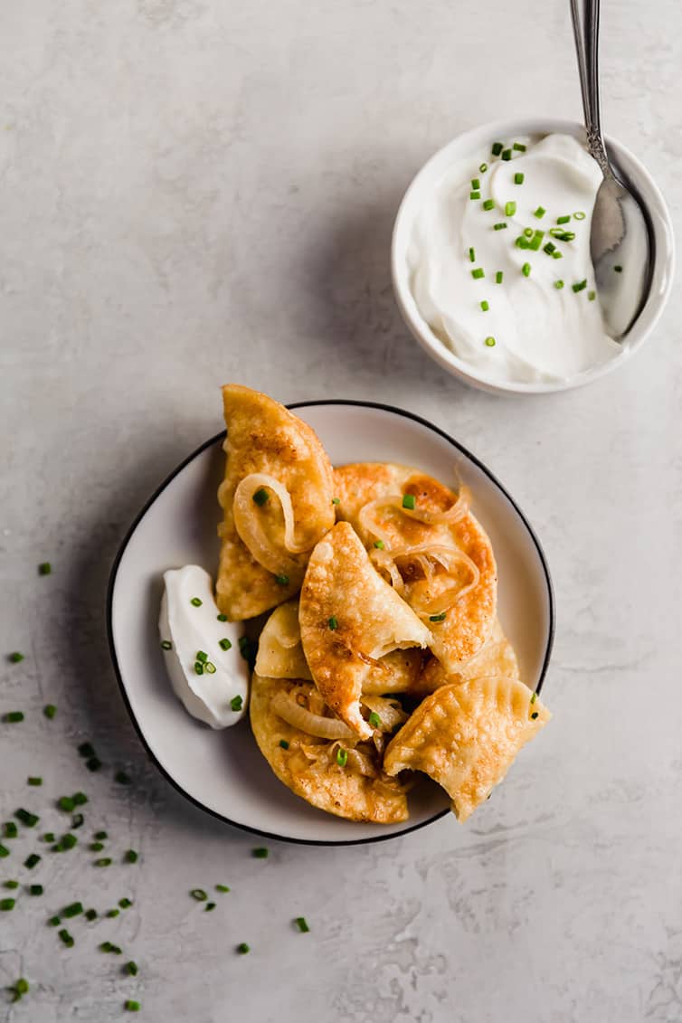 An overhead photo of a plate of pierogies served with sour cream.