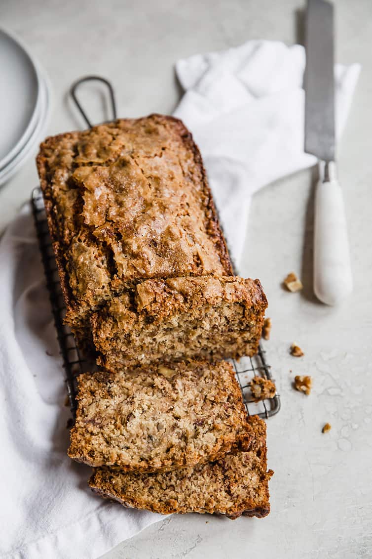 A loaf of banana bread on a wire rack with a few slices cut off.