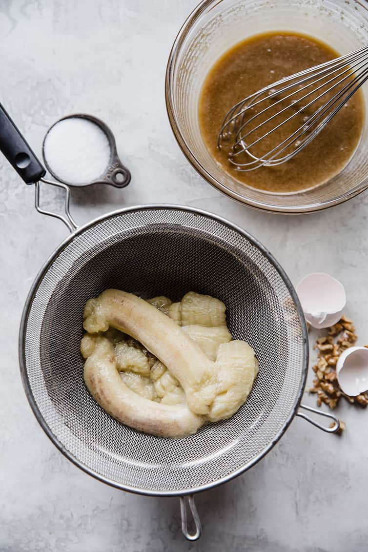 Bananas in a fine mesh strainer over a bowl.