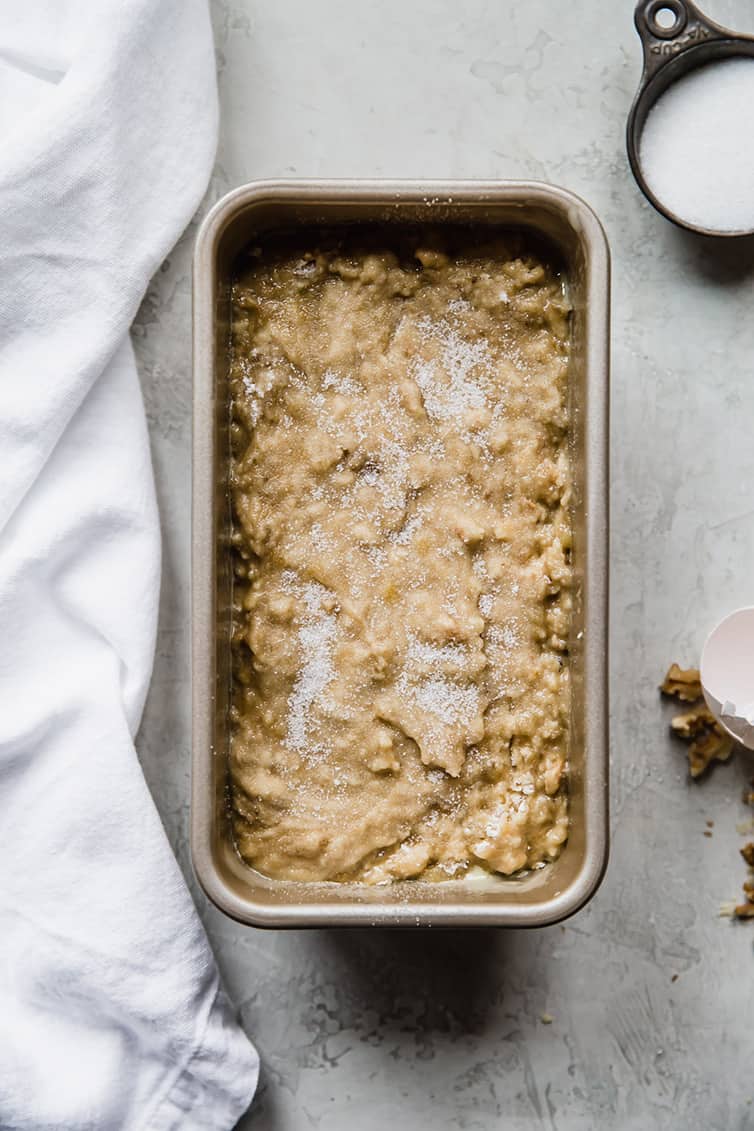 Banana bread batter in a loaf pan with sugar sprinkled on top.
