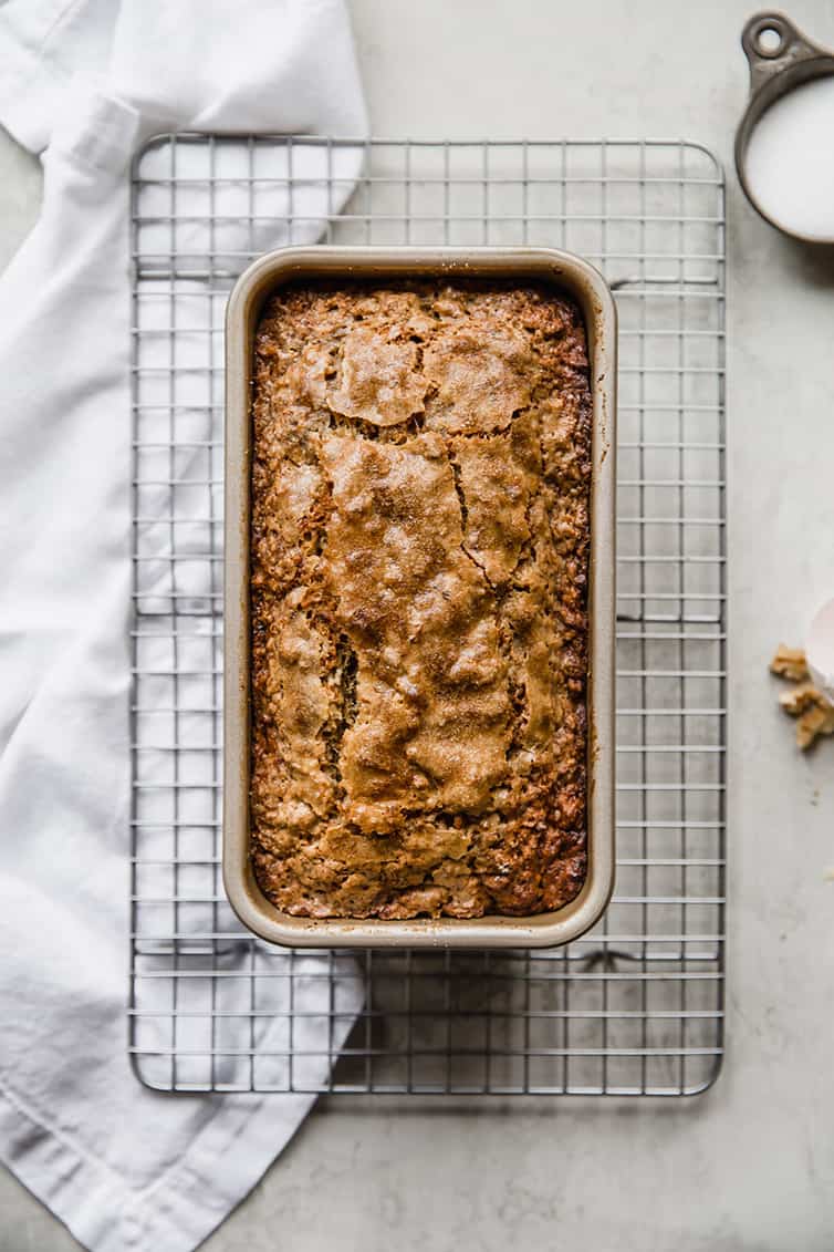 A baked loaf of banana bread still in the loaf pan on a wire rack.