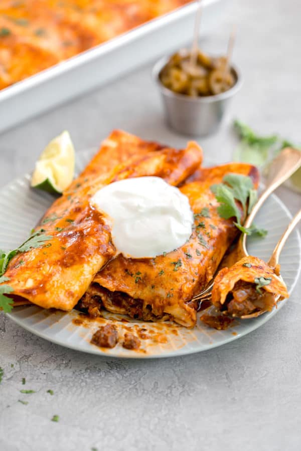 Two beef enchiladas on a plate, with a fork cut into one.