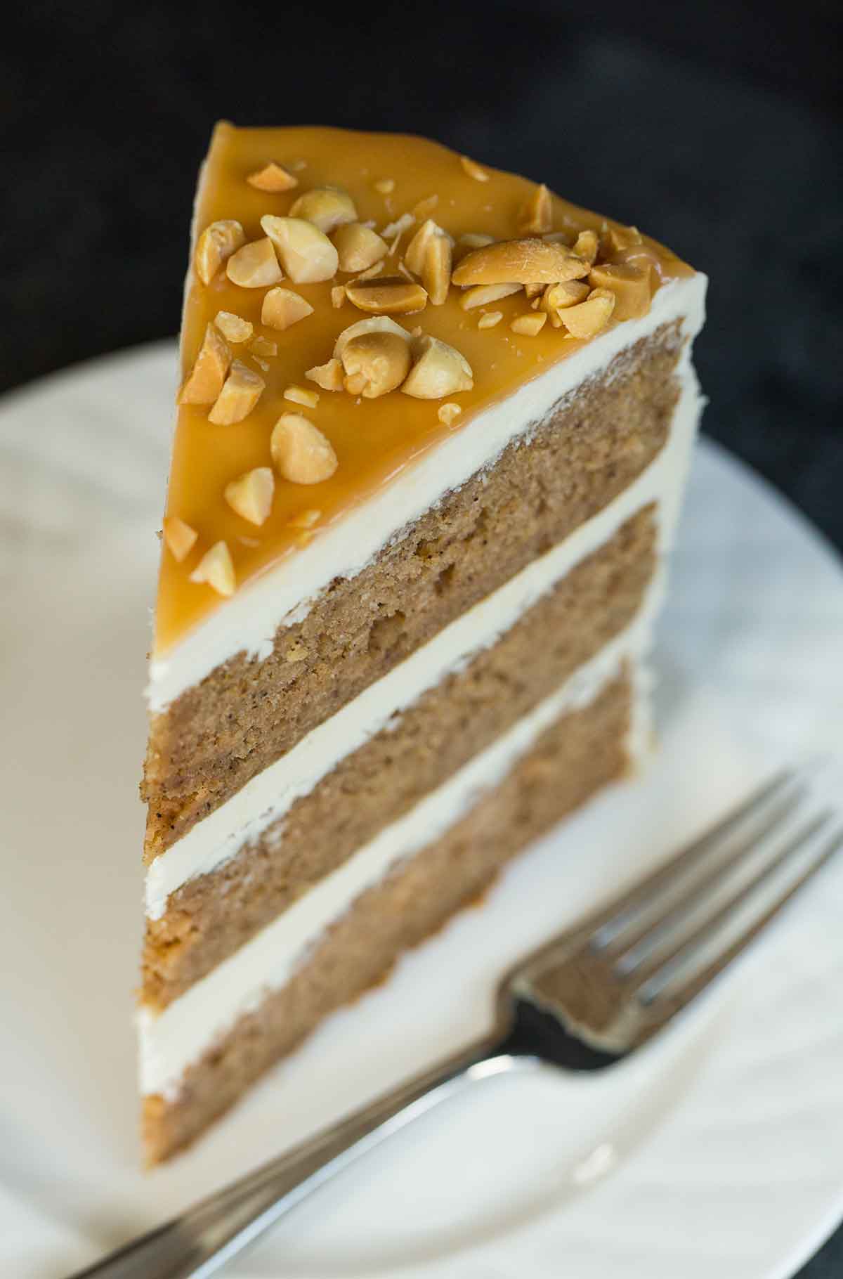 Slice of salted caramel apple cake with caramel glaze and chopped peanuts on top.
