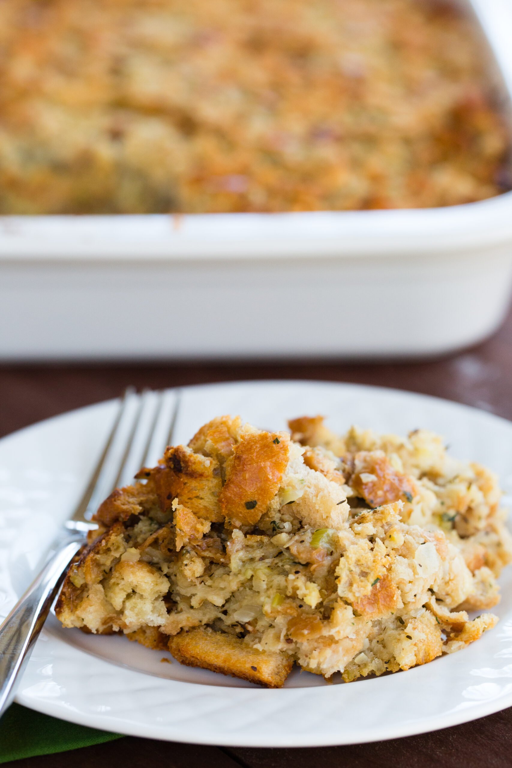 A plate of traditional bread stuffing with the whole pan in the background.