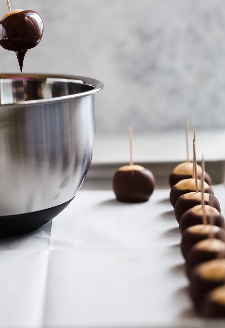 Dipping a buckeye into chocolate with finished ones on a pan.