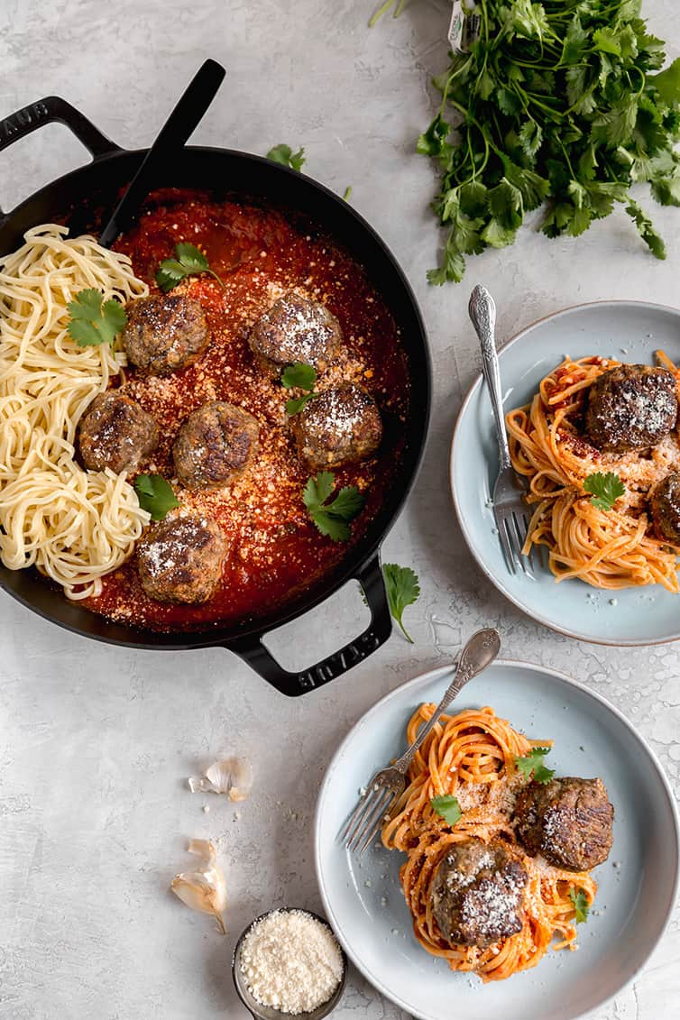 A pot of sauce with meatballs and spaghetti, with two plated servings next to it.