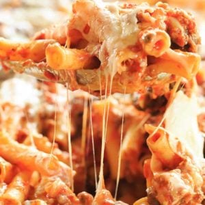 A spoonful of baked ziti being scooped out the pan.
